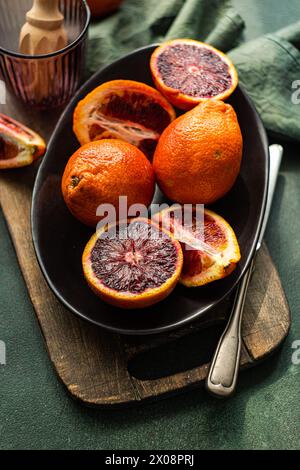 Juicy blood oranges arranged on a black ceramic plate against a rustic wooden board with a green fabric backdrop Stock Photo