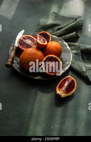 Fresh blood oranges on a dark plate with rustic knife and green cloth Stock Photo
