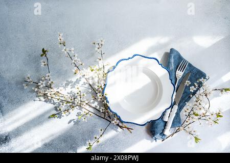 Elegant spring table setting engulfed in soft natural light, featuring cherry blossom branches and a classic white plate with blue trim Stock Photo