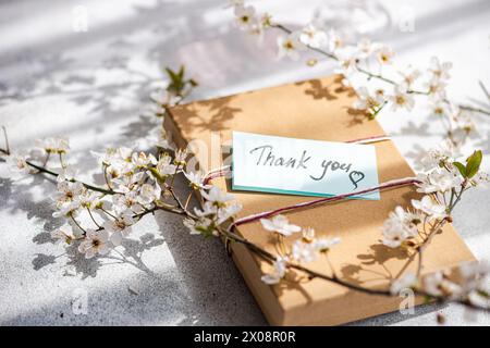 A craft paper envelope with a Thank you card, surrounded by delicate cherry blossoms in soft sunlight Stock Photo