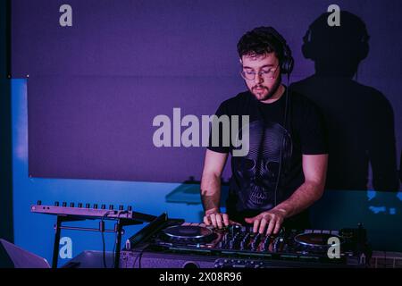 Concentrated male DJ mixing tracks on turntables with a shadow silhouette in the background at a club Stock Photo