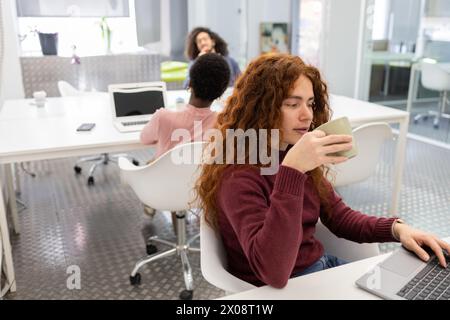 Diverse team in a modern office space with a young red-haired woman in the foreground. Stock Photo