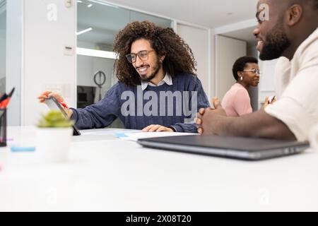 A Middle Eastern man smiles and works with his Black colleagues in a bright office setting, showing teamwork and collaboration. Stock Photo