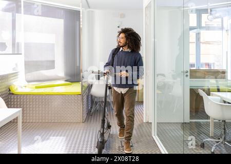 Professional African American man with a scooter in a modern office setting, looking away from the camera. Stock Photo