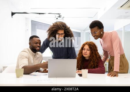 Diverse team of colleagues engaging in a project discussion around a laptop in a modern office setting. Two African American men and women, and two in Stock Photo