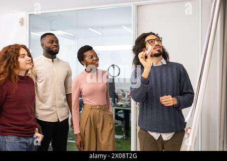 A diverse team in a corporate setting, with a man writing on a whiteboard. Stock Photo