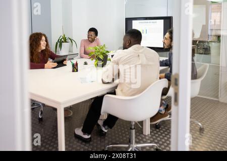 Diverse team of professionals engaged in a meeting with sales presentation in the background. Stock Photo