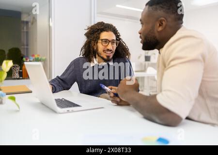 Two men engaged in a professional discussion at an office desk, looking at each other with focus and interest. Stock Photo
