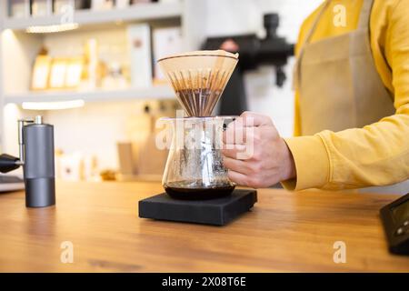 A close-up of a barista's hand pouring hot water through a coffee filter into a carafe at a stylish coffee shop. Stock Photo