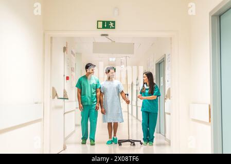 Male and female doctors walking with patient in hall of hospital. Stock Photo