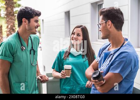 Group of men and woman in medical uniform standing and drinking coffee outdoors. Stock Photo