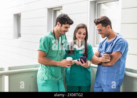 Group of medical workers browsing smartphone and drinking coffee during the break. Stock Photo