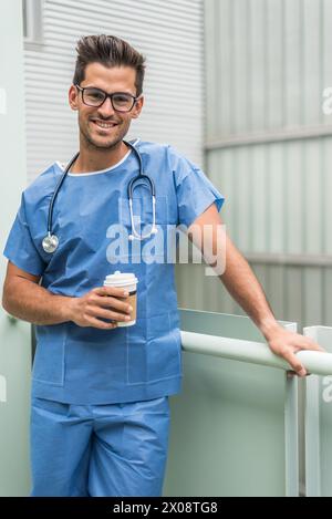 Smiling male medic looking at camera standing outside and having coffee. Stock Photo