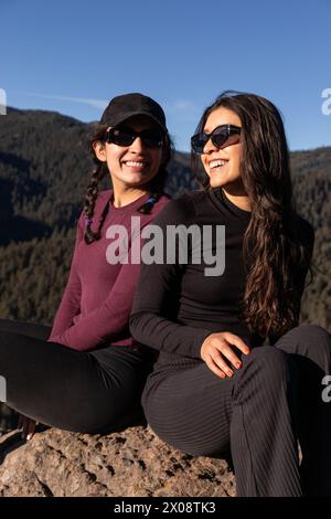 Two friends share a laugh while sitting on a rock, basking in the beauty of the mountainous landscape Stock Photo
