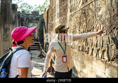 A local guide explains historical bas-reliefs to an attentive female tourist at Angkor Wat temple in Siem Reap, Cambodia. Stock Photo
