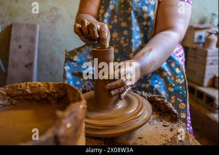 A skilled female artisan creates a clay pot on a spinning pottery wheel, showcasing the traditional craft of pottery-making. Stock Photo
