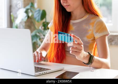 Anonymous redheaded woman books a nature getaway using a laptop and credit card at a cozy home setting Stock Photo