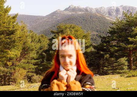 A redheaded woman with a serene expression is foregrounded against a lush mountainous landscape, embodying the tranquility of a nature getaway Stock Photo