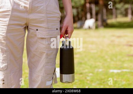 Captured in nature, anonymous woman enjoys a sunny getaway, holding a practical and reusable water bottle, ready for a day of adventure outdoors Stock Photo
