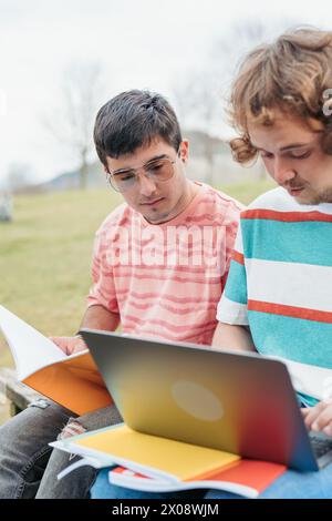 Two transgender men, a loving gay couple, are engrossed in their studies, surrounded by books and a laptop in a tranquil park Stock Photo