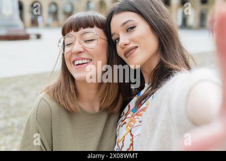 Two joyful women in stylish spring fashion taking a close-up selfie with genuine smiles Stock Photo