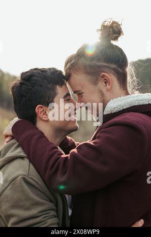Two men share a joyful embrace, with faces close together and smiles that speak of deep connection and happiness in their relationship Stock Photo