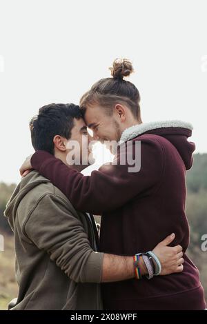Two men share a joyful embrace, with faces close together and smiles that speak of deep connection and happiness in their relationship Stock Photo
