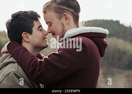 Two men share a joyful embrace, with faces close together and smiles that speak of deep connection and happiness in their relationship Stock Photo