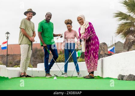 A group of four diverse friends is captured having a delightful time playing mini golf, with expressions of engagement and enjoyment. Stock Photo