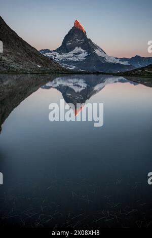 The iconic Matterhorn mountain peak is captured during twilight, reflecting in the tranquil waters of Riffelsee lake in Zermatt, Switzerland Stock Photo