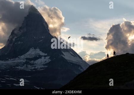 The Matterhorn looms over hikers and a paraglider in this serene scene of alpine adventure at dusk, showcasing the grandeur of nature Stock Photo