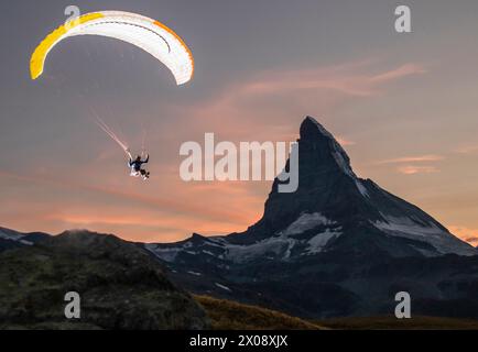 A paraglider soars against a scenic sunset backdrop with the majestic Matterhorn mountain towering in the distance Stock Photo