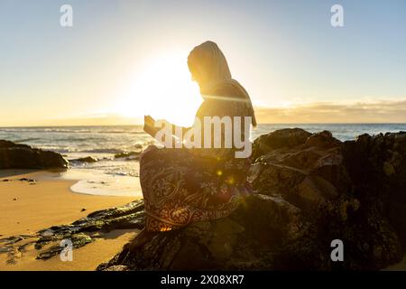 Serene Muslim woman reading at sunset on a beach Stock Photo