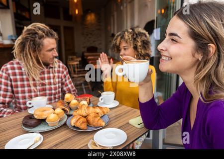 A group of friends is laughing and sharing a good time at a cafe, enjoying a selection of coffee and pastries Stock Photo