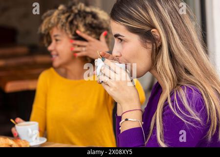 Two friends engage in a lively chat over coffee in a cozy cafe setting, with one sipping a beverage Stock Photo