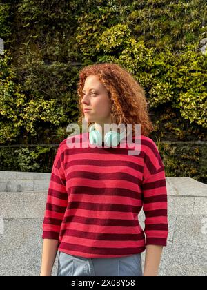 Young redhead woman with curly red hair wearing headphones outdoors Stock Photo