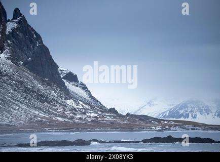 Majestic snow-covered mountains loom over a serene Icelandic landscape, with overcast skies adding a dramatic touch Stock Photo