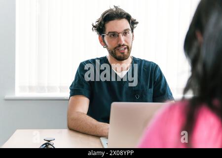 A friendly male doctor in scrubs is in a consultation, offering listening ear and advice to anonymous patient out of view Stock Photo