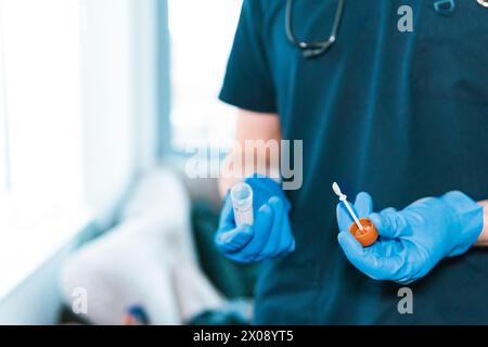 Close-up of anonymous medical practitioner's hands, gloved in blue, holding a sterile specimen container and applicator Stock Photo