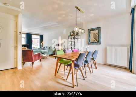 A contemporary living room with a dining table set for six, colorful chairs, and stylish lighting fixtures. Stock Photo