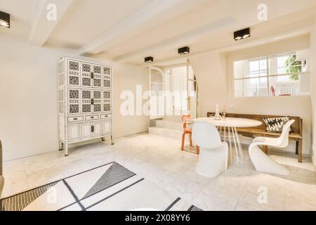 An elegant dining area featuring a round table, contemporary chairs, and an ornate white cabinet set against a bright interior. Stock Photo