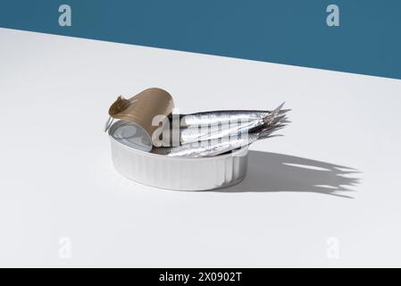 Gleaming fresh anchovies overflow from an unlidded tin can, set against a sharp blue and white divide, casting playful shadows Stock Photo