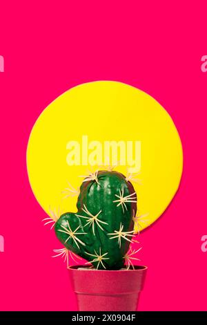 A vivid green cactus with white spikes is centered in front of a bright yellow circle, mimicking the sun on a hot pink background, giving a pop art fe Stock Photo
