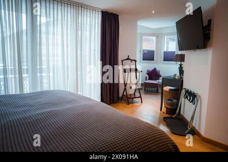 Luxury Hotel Room with Large Bed, Wooden Luggage Rack, and Flat Screen TV in Zermatt, Switzerland Stock Photo