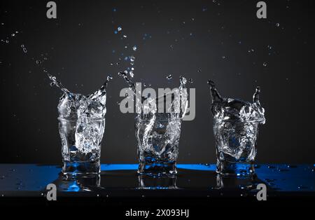 Alcoholic shots of vodka or strong drink in small glasses. A pieces of ice falls into a glasses, creating a splash. Copy space. Stock Photo
