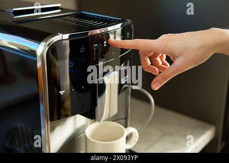 Woman preparing fresh cup of coffee with modern espresso machine. Female hand pressing button on coffee machine Stock Photo