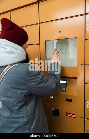 A young woman is entering a security code on a keypad to access an underground parking lot in the city center. The area is dimly lit, and the woman ap Stock Photo