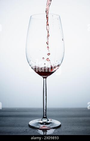 clear crystal glass with red sparkling cocktail served from above, liquid in motion, with the table splashed with liquid Stock Photo