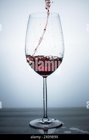 clear crystal glass with red sparkling cocktail served from above, liquid in motion, with the table splashed with liquid Stock Photo