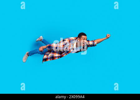 Full size photo of nice young man raise fist fly empty space wear shirt isolated on blue color background Stock Photo